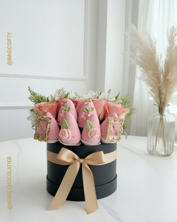 Box premium de fresas rosadas decoradas con flores y mariposas en caja cilíndrica negra con lazo dorado